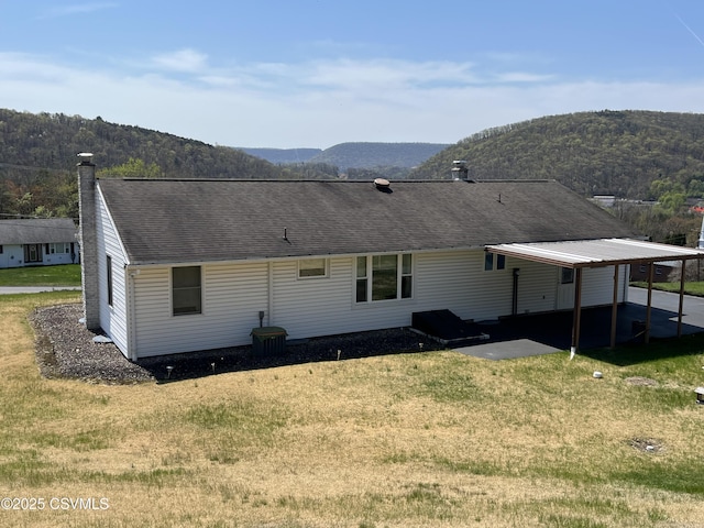rear view of property featuring a lawn, a mountain view, and a shingled roof