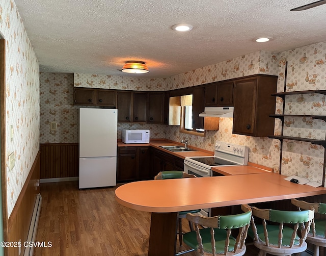 kitchen featuring wallpapered walls, under cabinet range hood, a sink, white appliances, and a textured ceiling