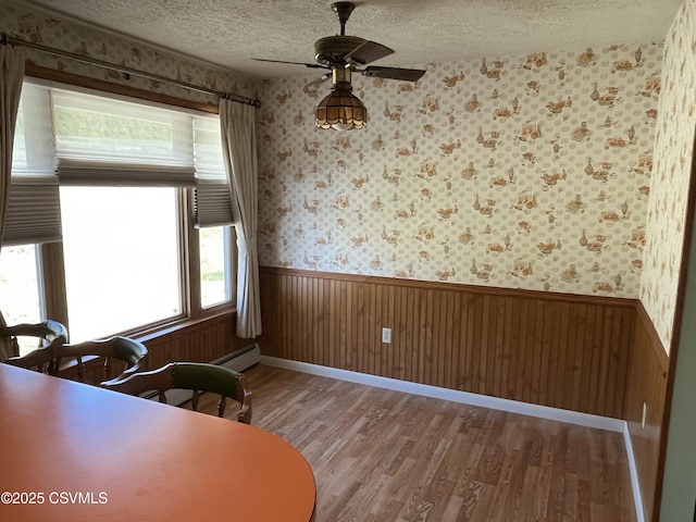 dining area featuring wallpapered walls, a wainscoted wall, wood finished floors, a textured ceiling, and ceiling fan