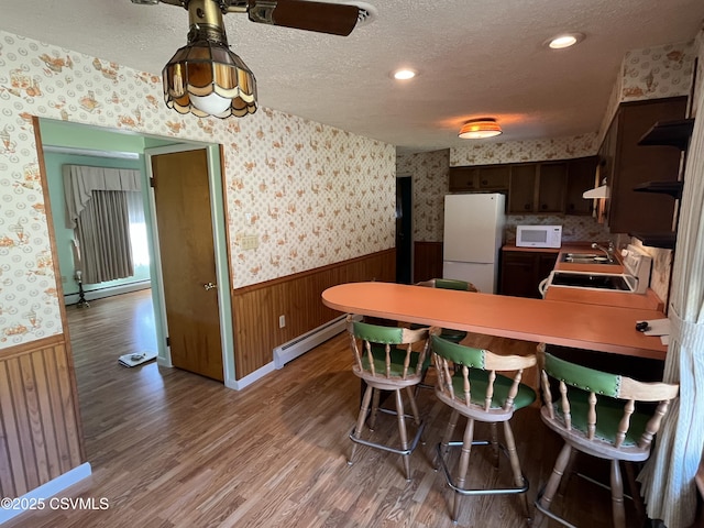 kitchen featuring wainscoting, wallpapered walls, white appliances, and a baseboard radiator
