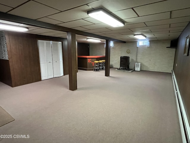 below grade area featuring baseboard heating, a drop ceiling, a dry bar, carpet, and wood walls