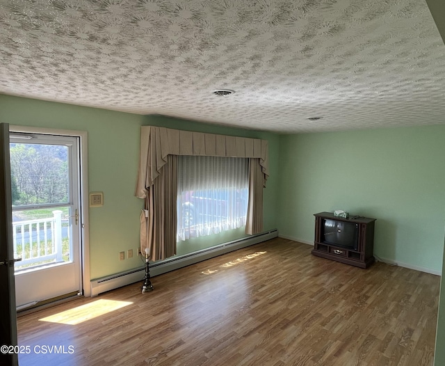 unfurnished living room with wood finished floors, a textured ceiling, and baseboard heating