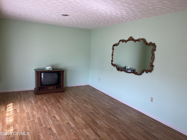 unfurnished living room with baseboards, wood finished floors, and a textured ceiling