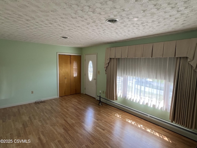entrance foyer featuring a textured ceiling, visible vents, baseboards, wood finished floors, and a baseboard radiator