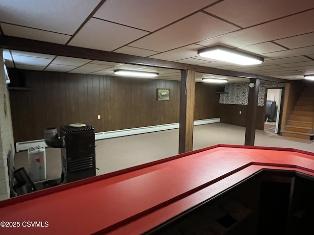 finished below grade area with stairway, wooden walls, heating fuel, a baseboard radiator, and a paneled ceiling