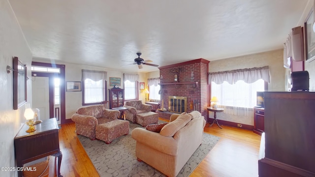 living area with light wood-type flooring, healthy amount of natural light, ceiling fan, and a fireplace