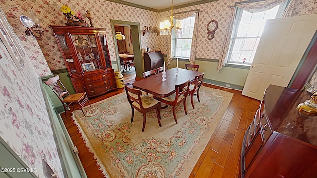 dining space with wallpapered walls, hardwood / wood-style floors, ornamental molding, a chandelier, and a wainscoted wall