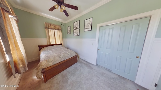 carpeted bedroom featuring wainscoting, a closet, crown molding, and ceiling fan