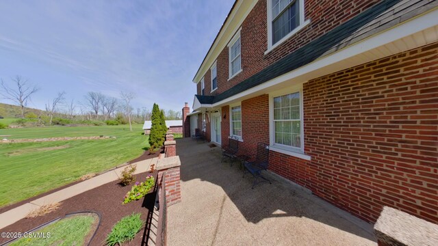 view of side of property featuring a yard, brick siding, and a patio area