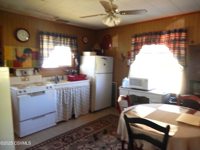 kitchen featuring wood walls, light tile patterned floors, white appliances, and ceiling fan