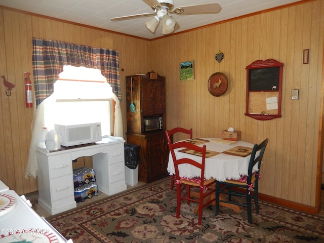 dining area featuring ornamental molding, ceiling fan, and wood walls