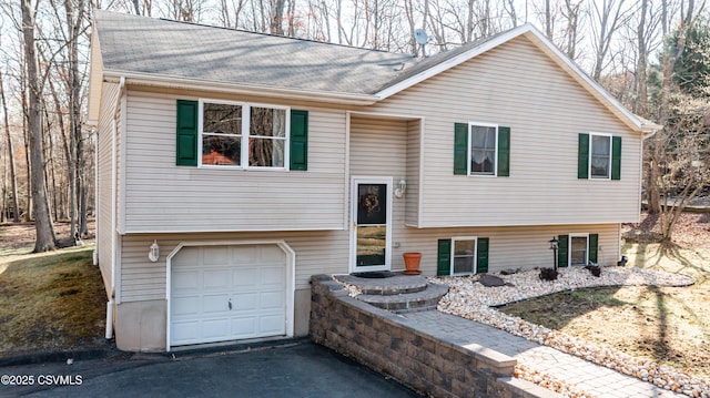 split foyer home featuring driveway, a garage, and roof with shingles