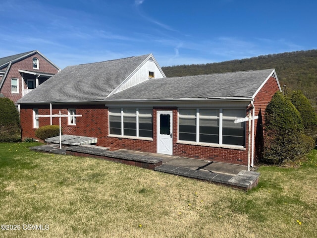 back of house with brick siding, roof with shingles, and a yard