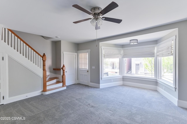 unfurnished living room featuring ceiling fan, carpet, stairs, baseboards, and a healthy amount of sunlight