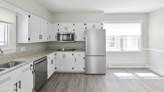 kitchen featuring appliances with stainless steel finishes, baseboard heating, light stone countertops, wood finished floors, and white cabinetry