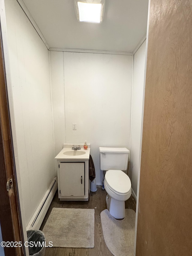 half bathroom with vanity, wood finished floors, baseboard heating, and toilet