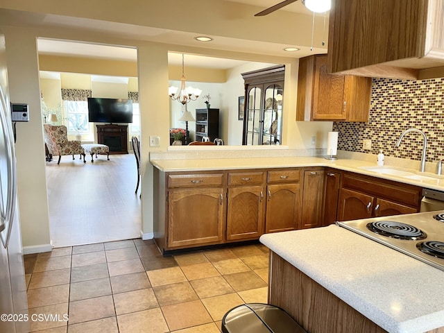 kitchen featuring brown cabinetry, light countertops, tasteful backsplash, a sink, and ceiling fan with notable chandelier