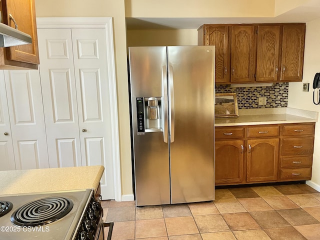 kitchen featuring brown cabinetry, stainless steel refrigerator with ice dispenser, light countertops, tasteful backsplash, and electric stove