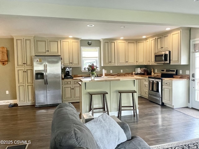kitchen with appliances with stainless steel finishes, cream cabinets, a center island, and dark wood finished floors