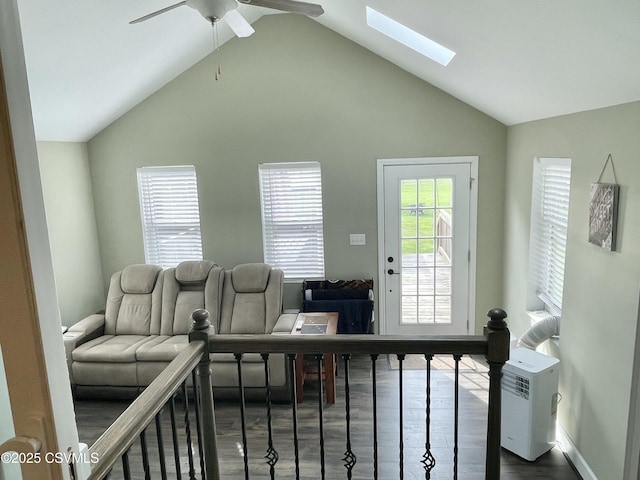 living room featuring dark wood-style flooring, a ceiling fan, baseboards, and vaulted ceiling with skylight