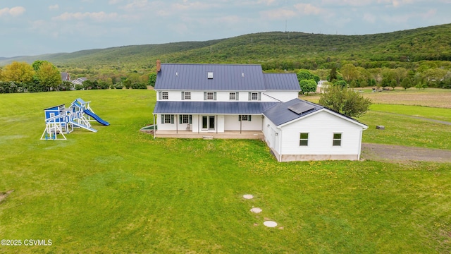 rear view of house with a lawn, a patio, a playground, and a wooded view