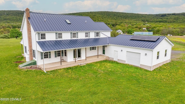 rear view of property with a standing seam roof, a chimney, a yard, and a garage