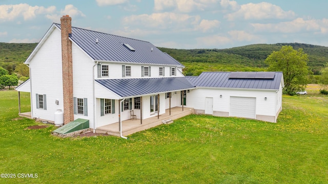 back of house with a standing seam roof, a chimney, metal roof, and a yard