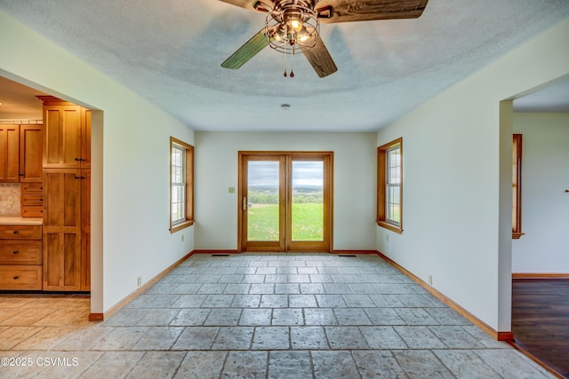empty room featuring ceiling fan, baseboards, stone tile flooring, and a textured ceiling