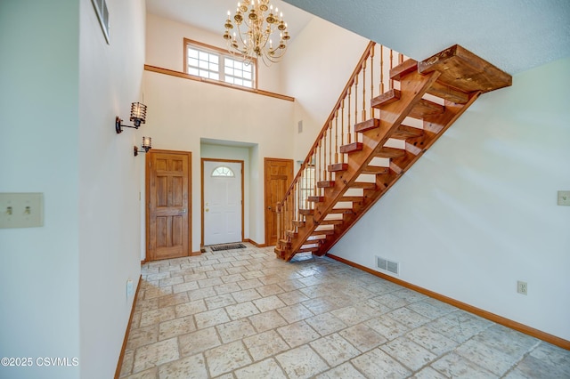 entrance foyer featuring baseboards, stairway, a chandelier, a high ceiling, and stone tile flooring