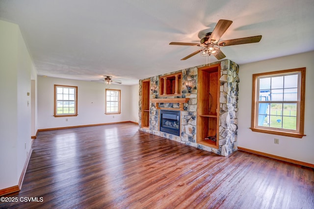 unfurnished living room with ceiling fan, wood finished floors, a stone fireplace, and baseboards