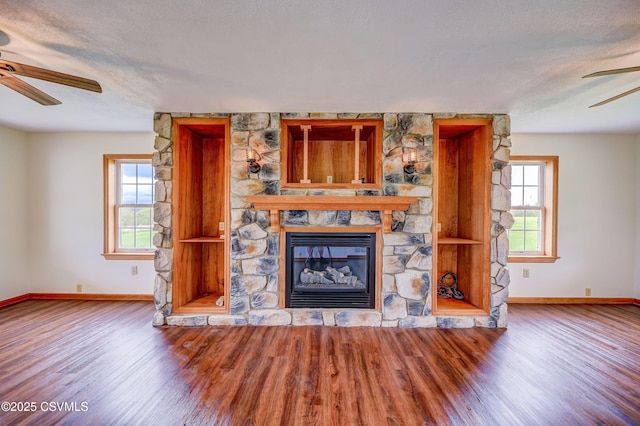unfurnished living room with ceiling fan, baseboards, wood finished floors, a fireplace, and a textured ceiling