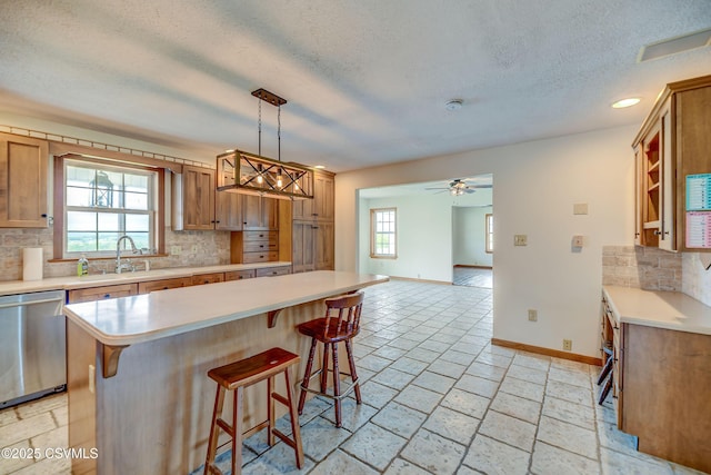 kitchen with a sink, dishwasher, a textured ceiling, light countertops, and baseboards