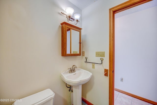 bathroom with toilet, tile patterned flooring, baseboards, a textured ceiling, and a sink