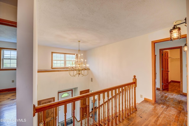 corridor featuring an upstairs landing, hardwood / wood-style flooring, a textured ceiling, a chandelier, and baseboards