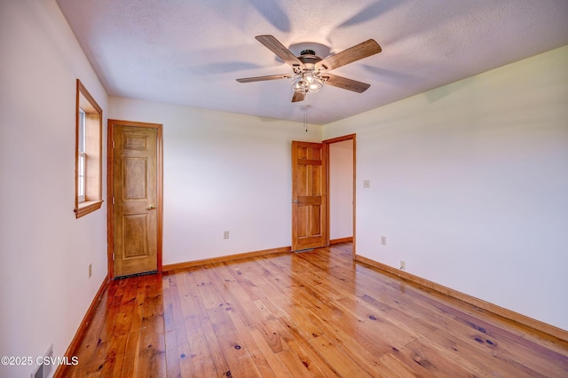 unfurnished room with a ceiling fan, light wood-style floors, baseboards, and a textured ceiling