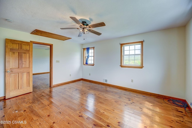 unfurnished room with attic access, a ceiling fan, baseboards, light wood finished floors, and a smoke detector