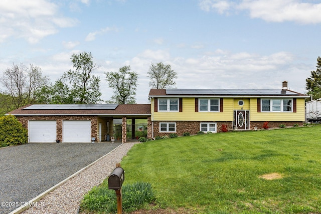 view of front of property featuring solar panels, a front yard, a garage, gravel driveway, and brick siding