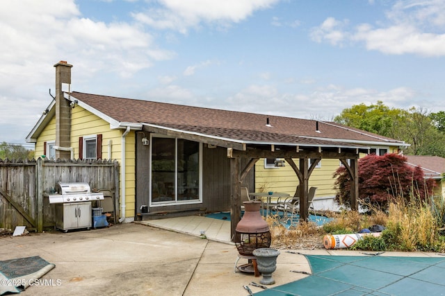 back of house with roof with shingles, fence, a wooden deck, a patio area, and a chimney