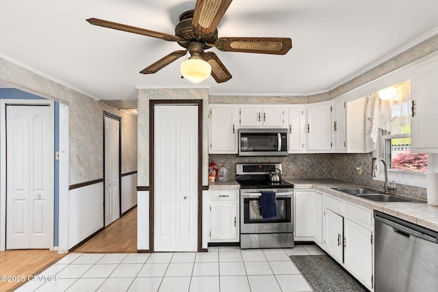 kitchen with stainless steel appliances, a sink, ornamental molding, white cabinetry, and light tile patterned flooring