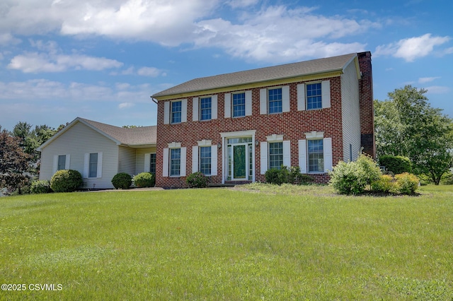 colonial house featuring brick siding, a front yard, and a chimney