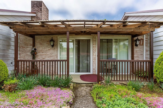 entrance to property featuring brick siding, a chimney, covered porch, and a pergola