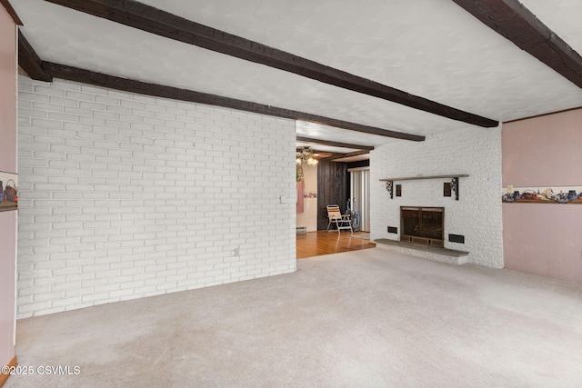 unfurnished living room featuring beam ceiling, carpet, a fireplace, brick wall, and a ceiling fan