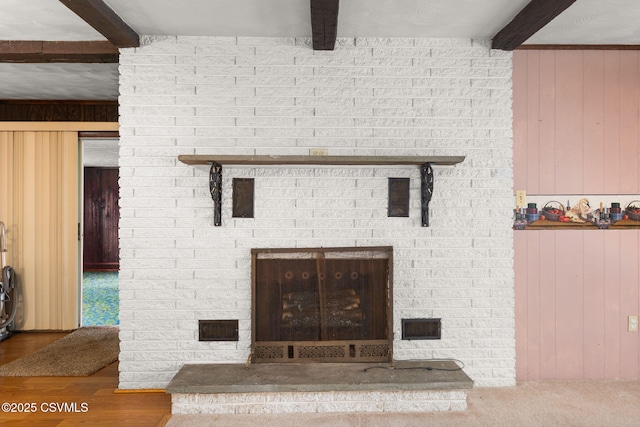 detailed view of beam ceiling, wood walls, a brick fireplace, and wood finished floors
