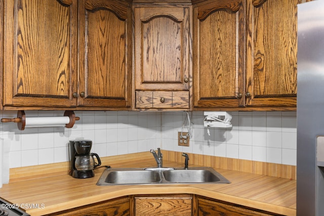 kitchen with a sink, decorative backsplash, butcher block counters, and brown cabinetry
