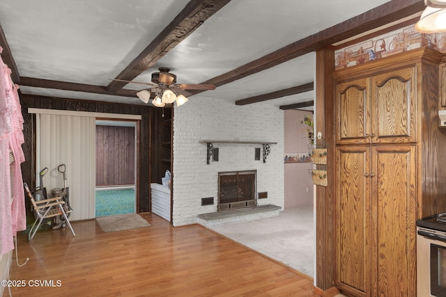 living area with a ceiling fan, light wood-style floors, beam ceiling, and a brick fireplace
