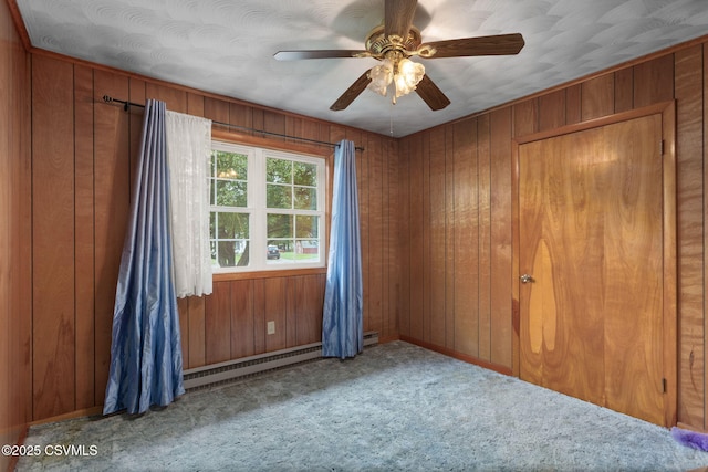 carpeted spare room with wooden walls, a ceiling fan, baseboards, and a baseboard radiator