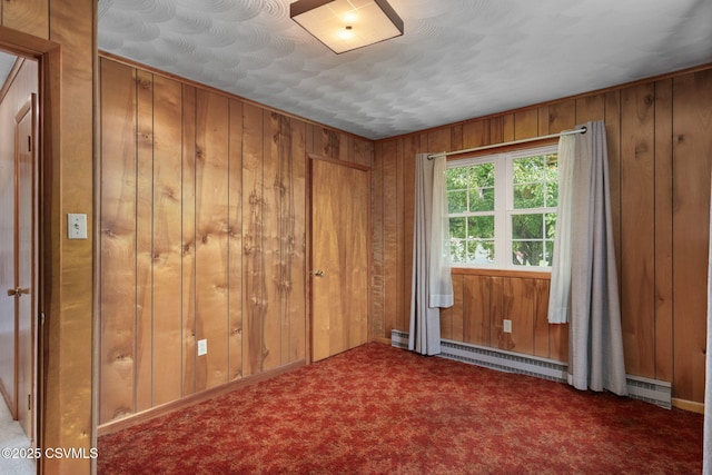 carpeted spare room with wood walls and a baseboard radiator
