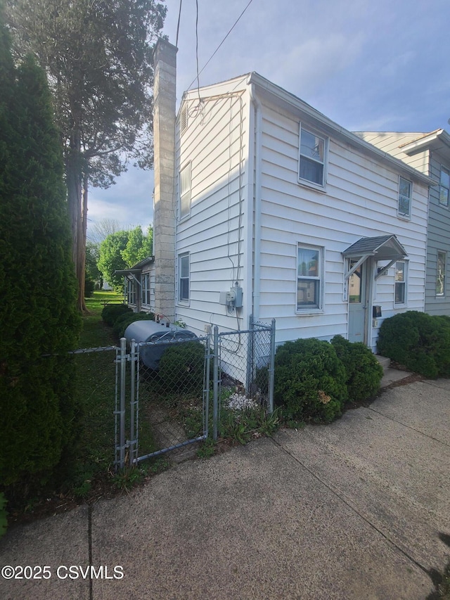 view of side of property with a gate, a chimney, and fence