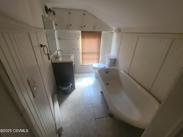bathroom with a bathtub, vanity, vaulted ceiling, toilet, and tile patterned flooring