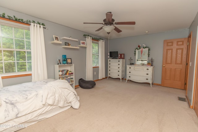 bedroom with multiple windows, light colored carpet, a ceiling fan, and baseboards